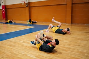 a couple of men laying on top of a basketball court