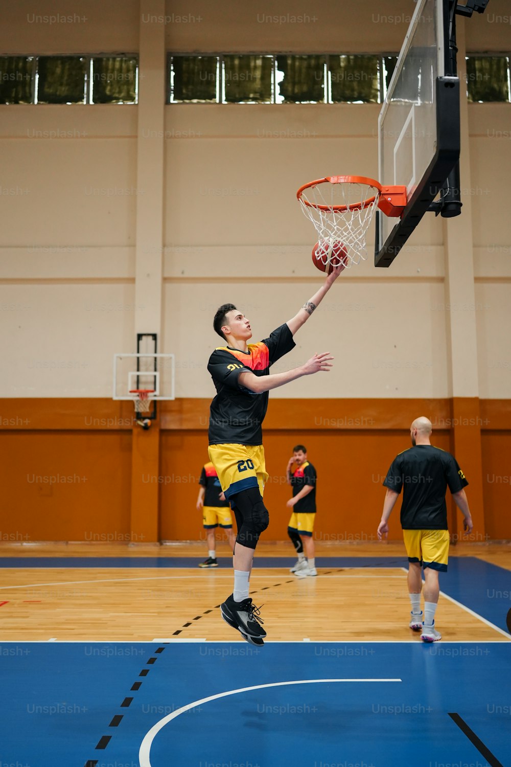 Un hombre con camisa negra y pantalones cortos amarillos jugando baloncesto
