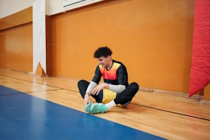 a young man sitting on the floor tying his shoes