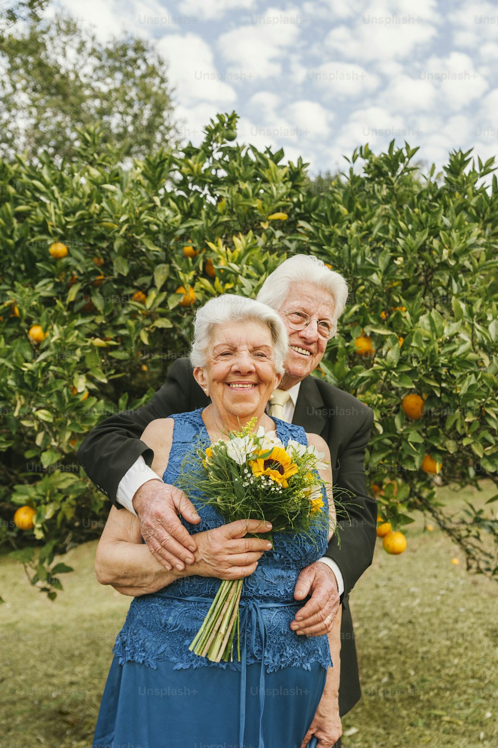 um casal mais velho abraçando-se em frente a uma laranjeira