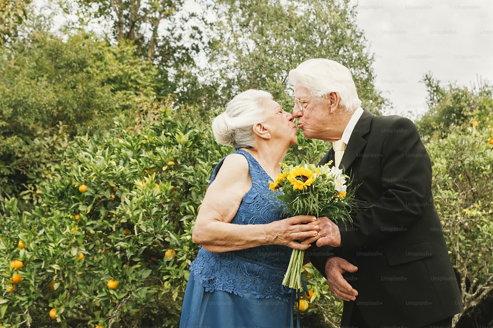 an older couple kissing each other in front of trees