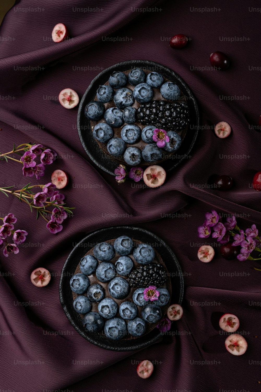 a bowl of blueberries and a bowl of cherries on a purple cloth