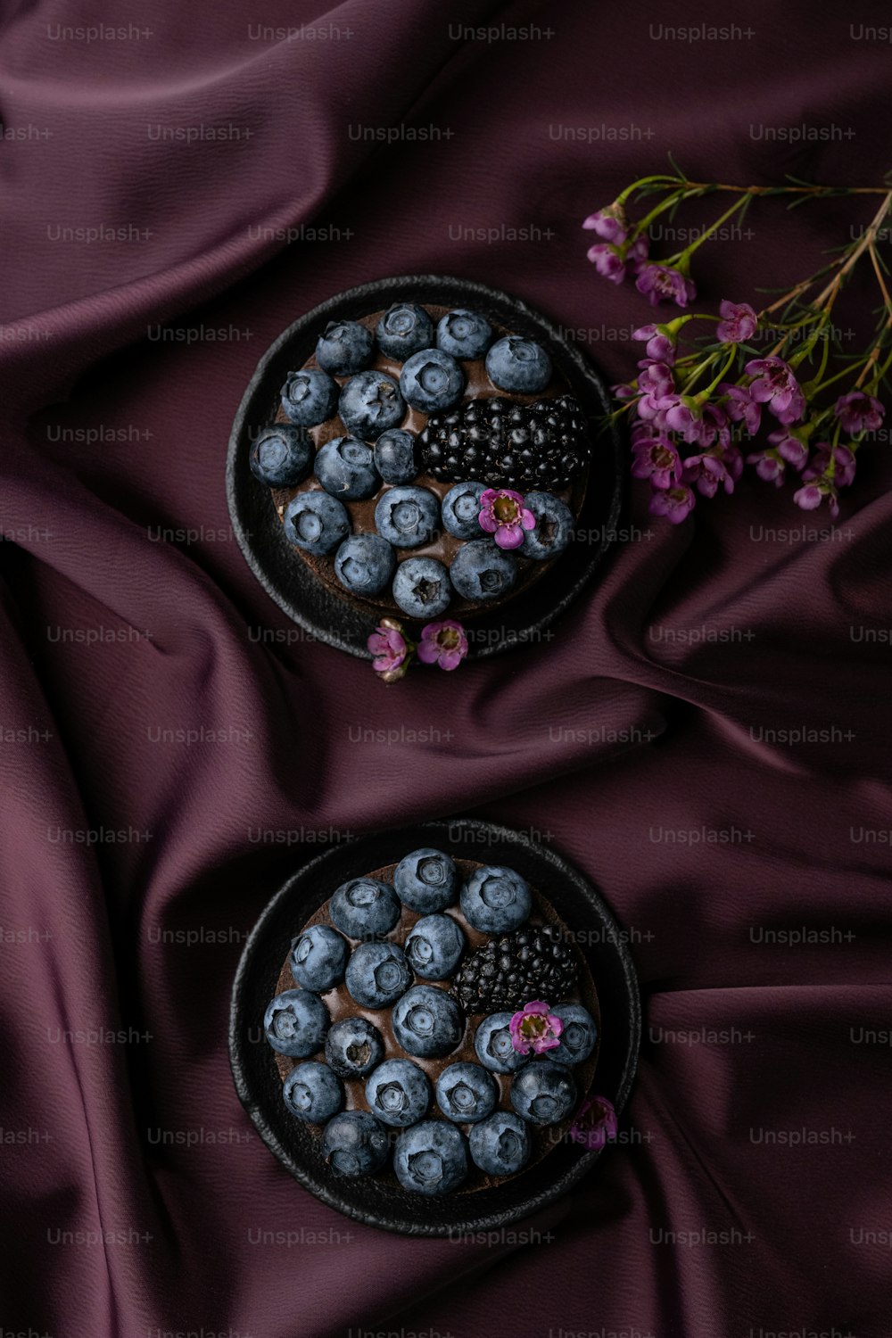 two plates of blueberries on a purple cloth