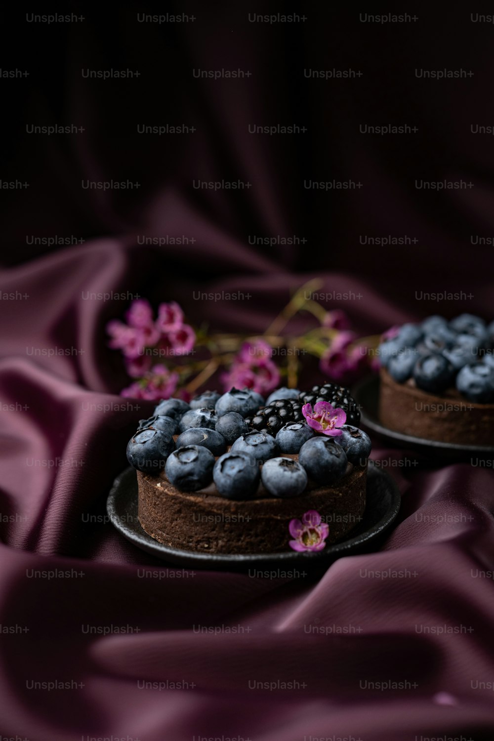 two cakes with blueberries and blackberries on a purple cloth