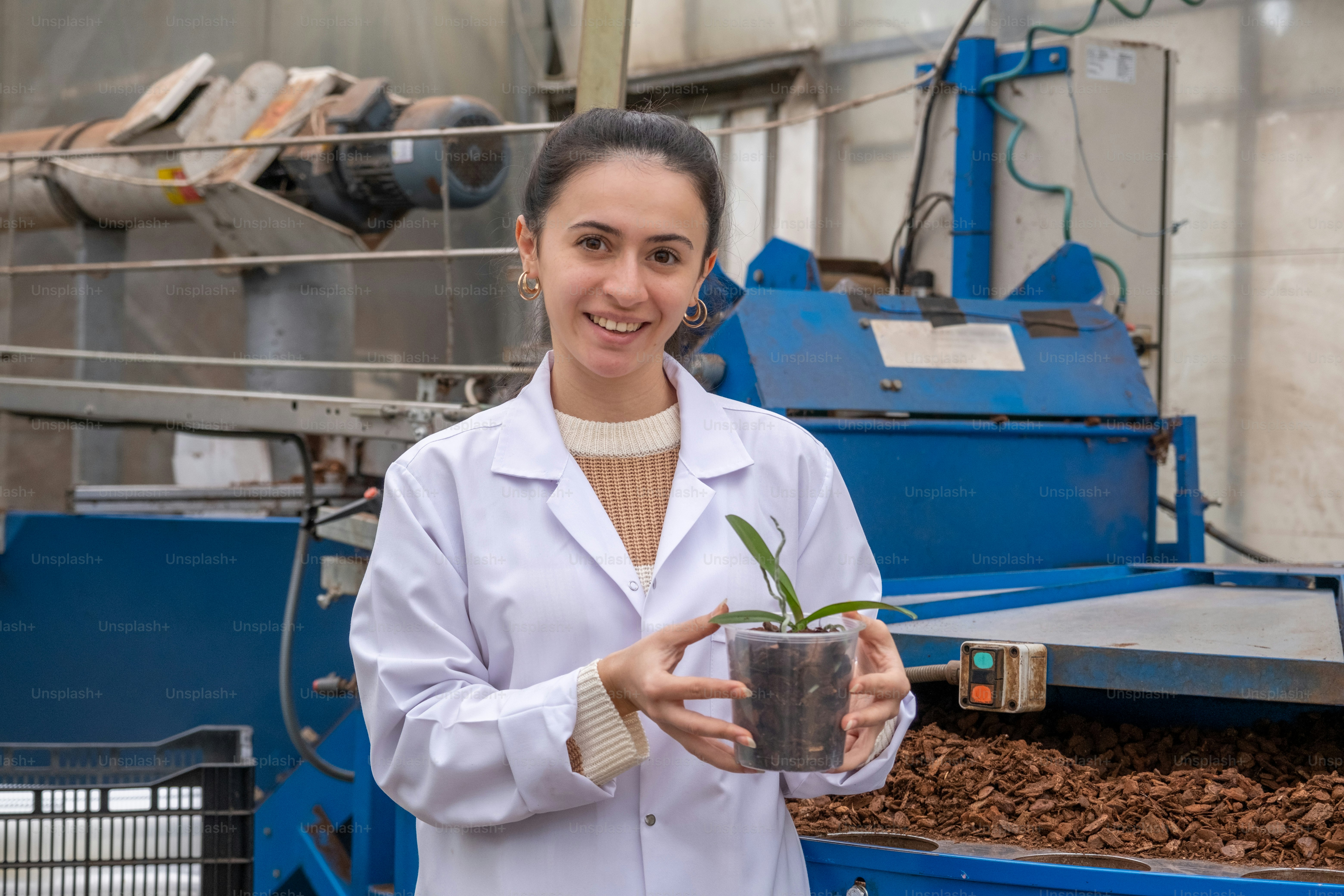 Una mujer con una bata de laboratorio sosteniendo una planta en maceta