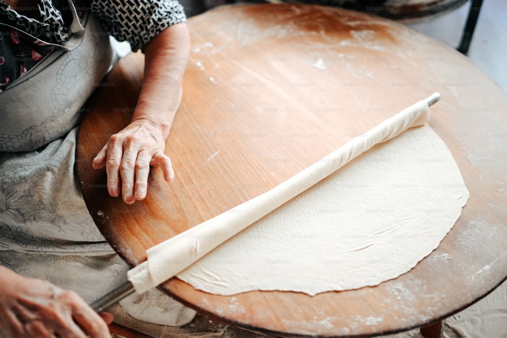 a woman rolling out dough on top of a wooden table