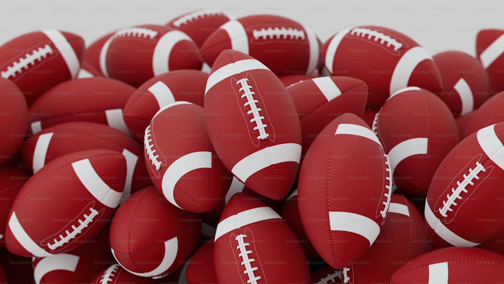 a pile of red leather footballs with white stitching