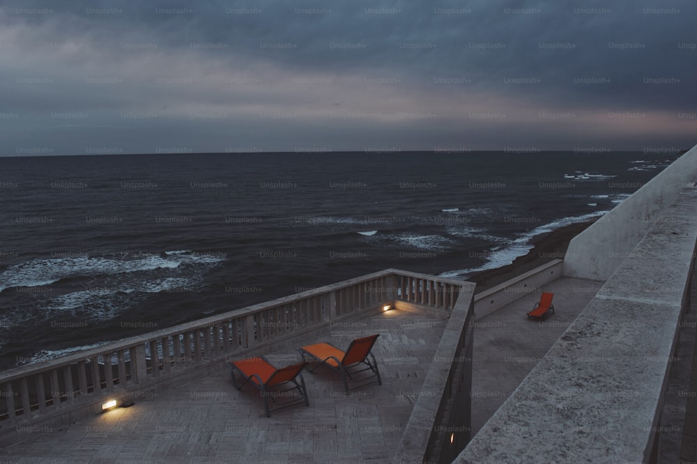 a couple of chairs sitting on top of a balcony next to the ocean