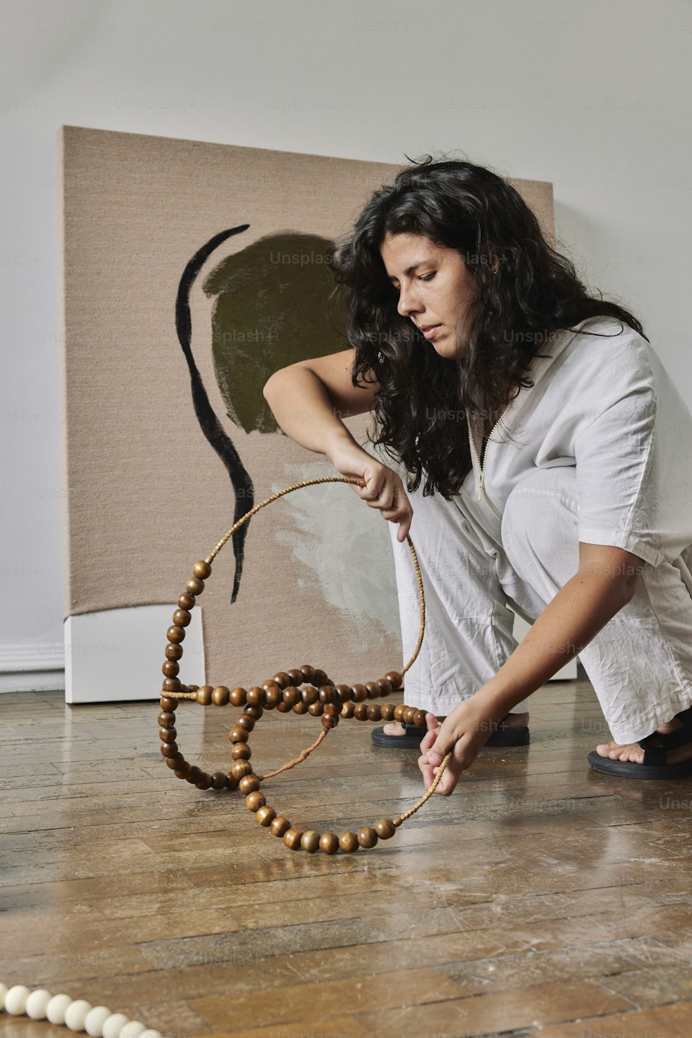 a woman kneeling down on the floor with a wooden beaded object