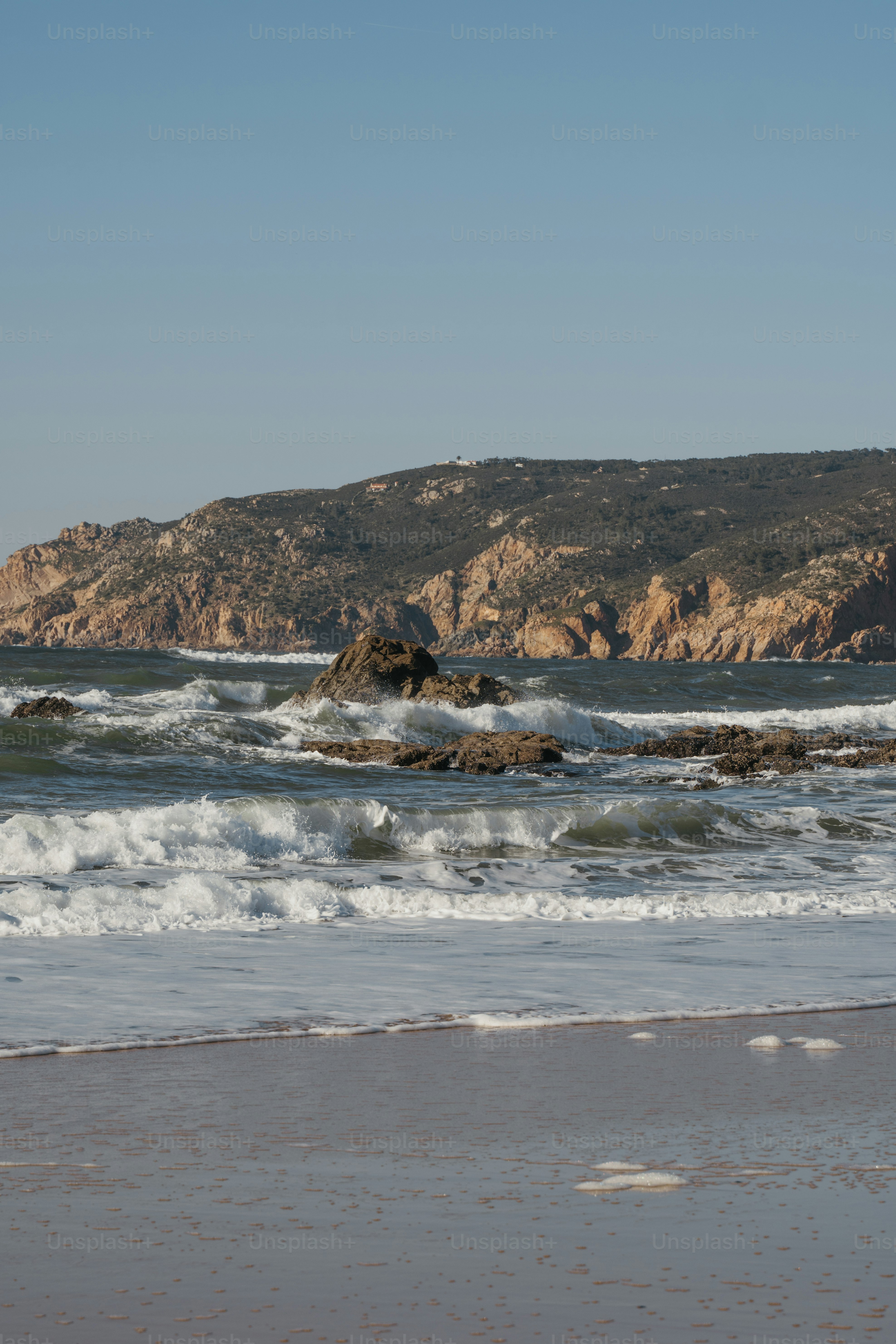 a beach with waves coming in to shore and a mountain in the background