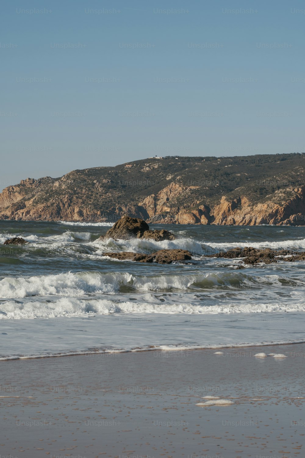 une plage avec des vagues arrivant sur le rivage et une montagne en arrière-plan