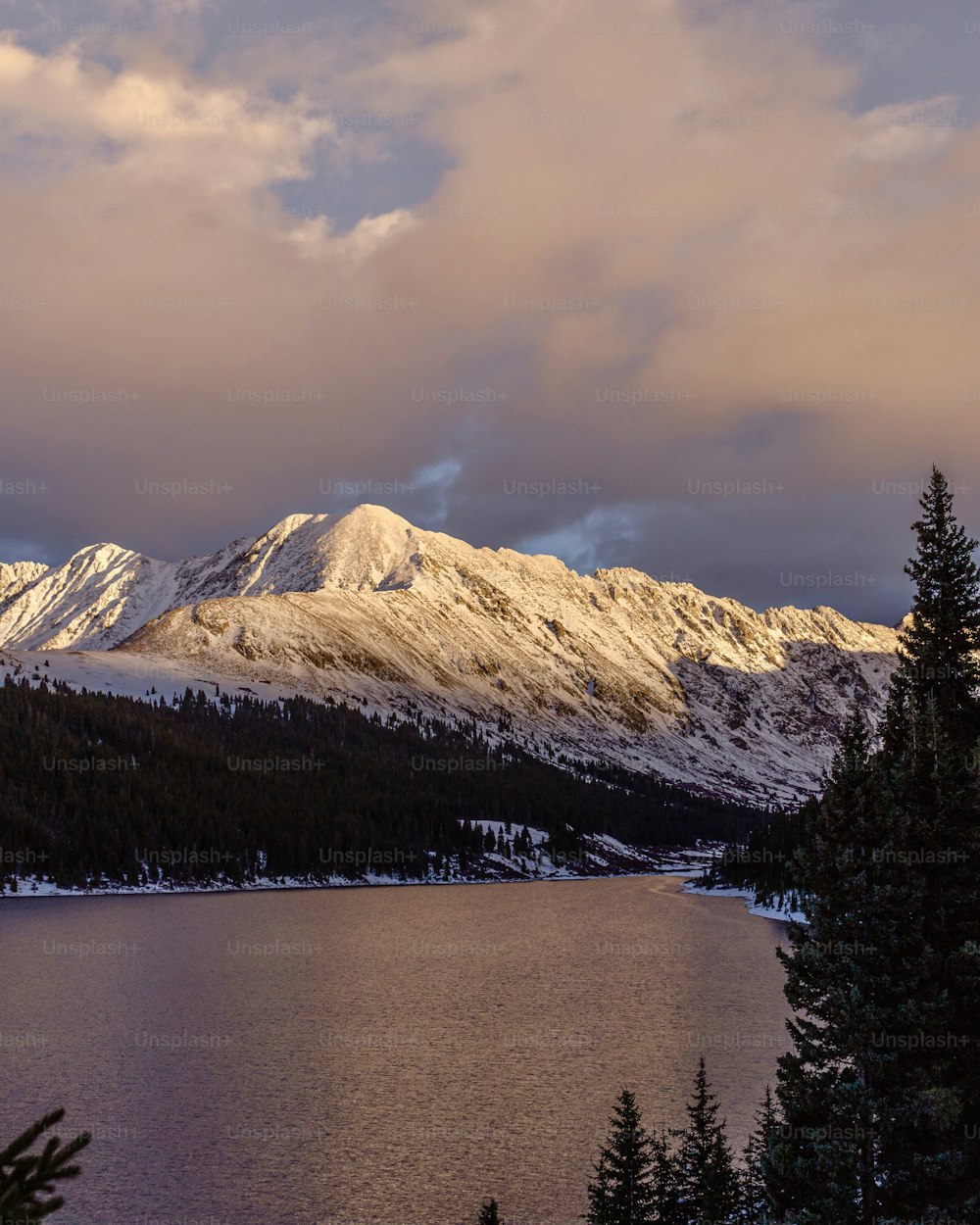 a lake surrounded by snow covered mountains under a cloudy sky