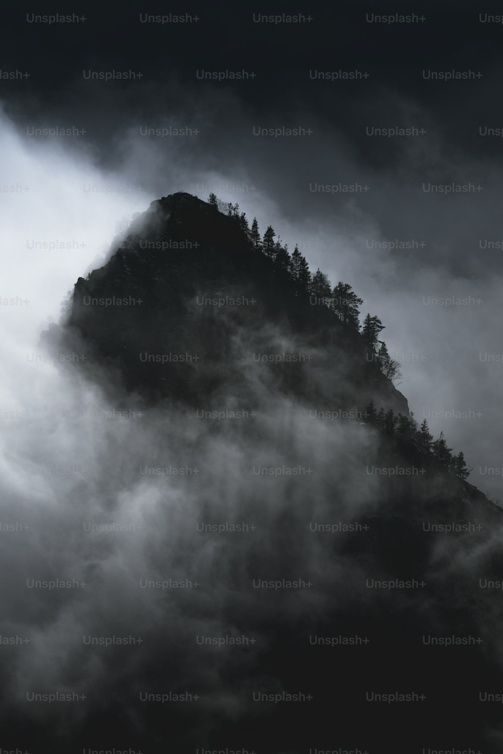 a black and white photo of a mountain covered in clouds