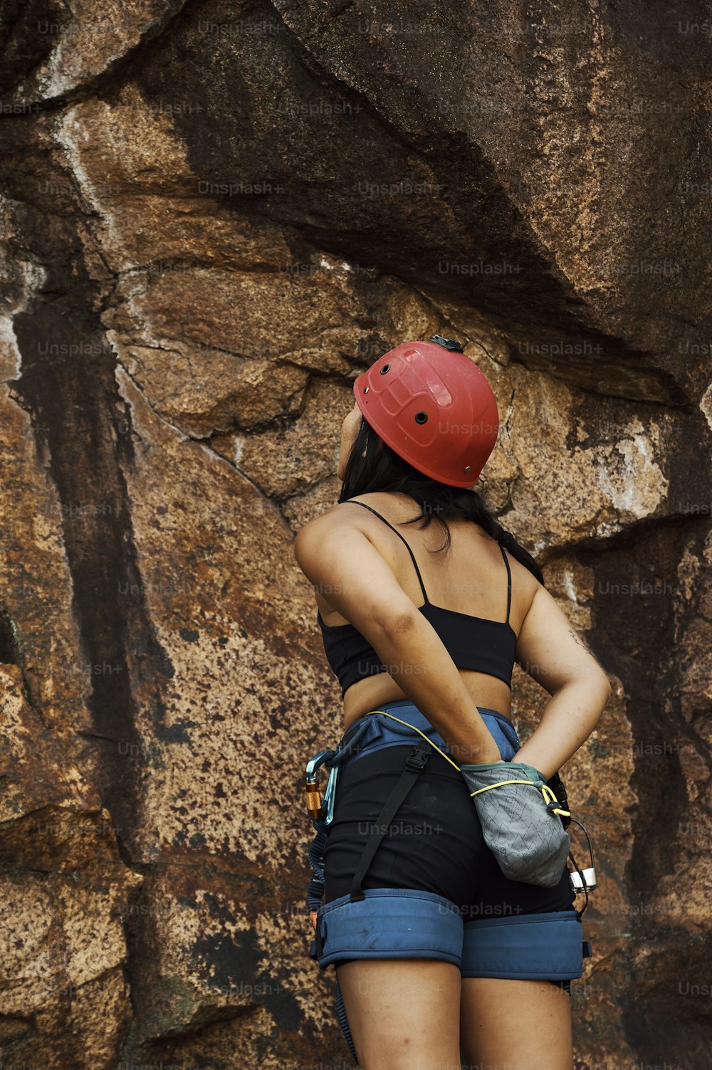a woman wearing a red helmet standing in front of a rock