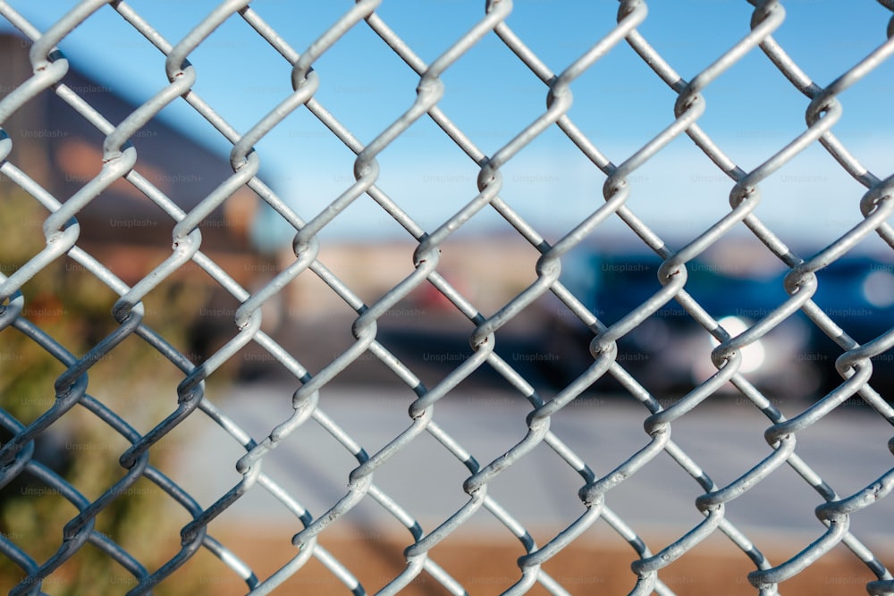 a chain link fence with a parking lot in the background