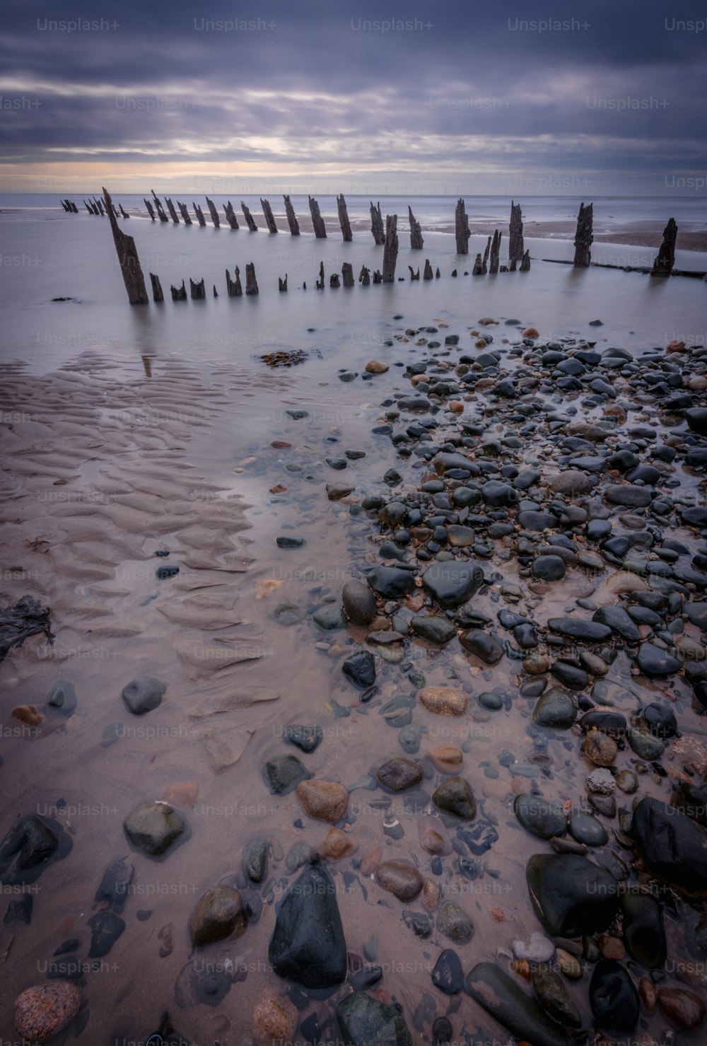 uma praia com pedras e postes saindo da água
