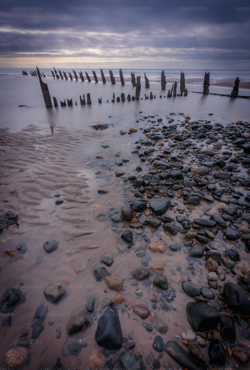 a beach with rocks and poles sticking out of the water