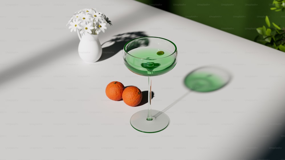 a glass of green liquid next to two oranges