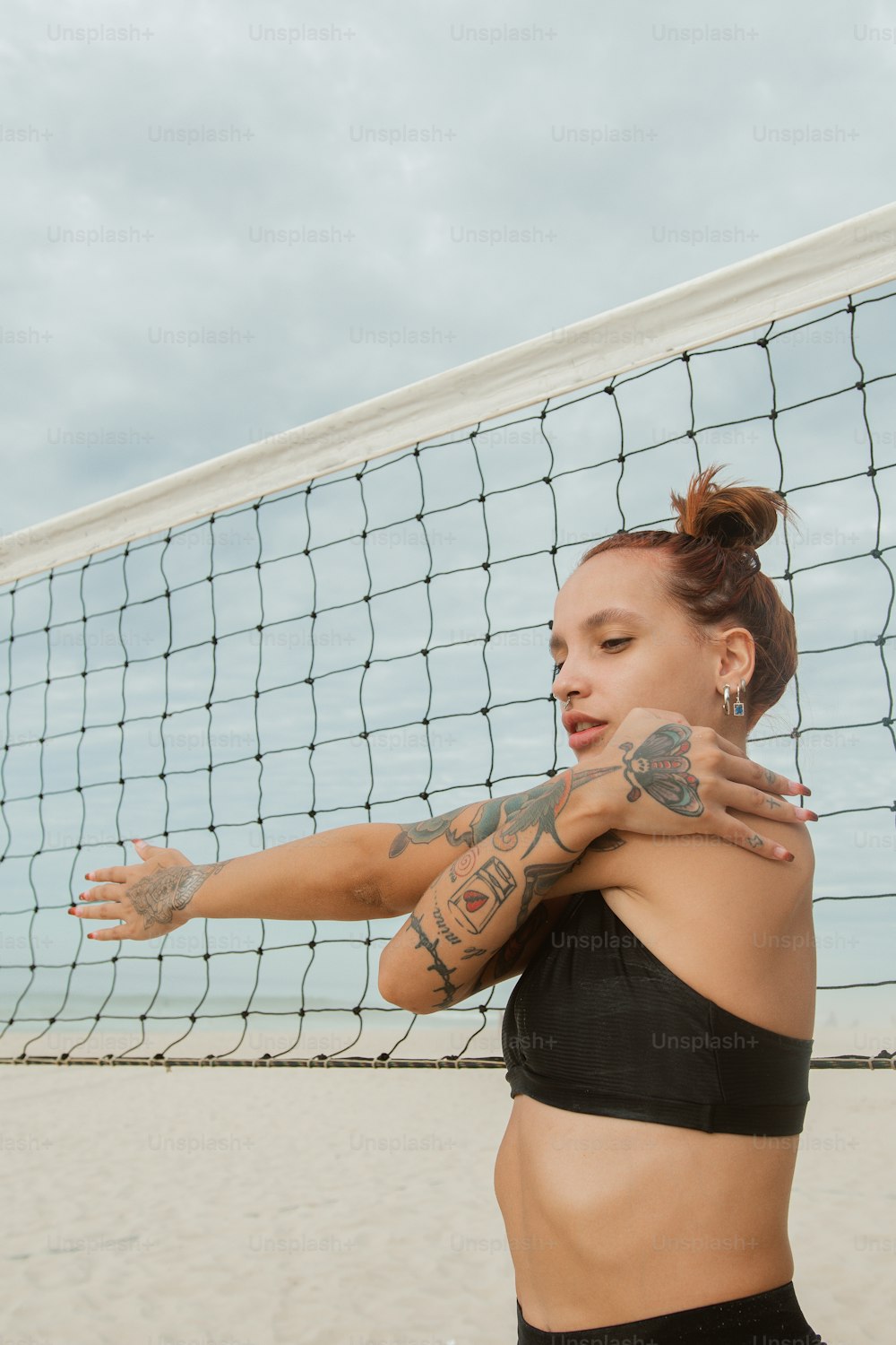 a woman with tattoos on her arm standing in front of a volleyball net