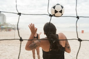 a woman standing on a beach with a soccer ball above her head