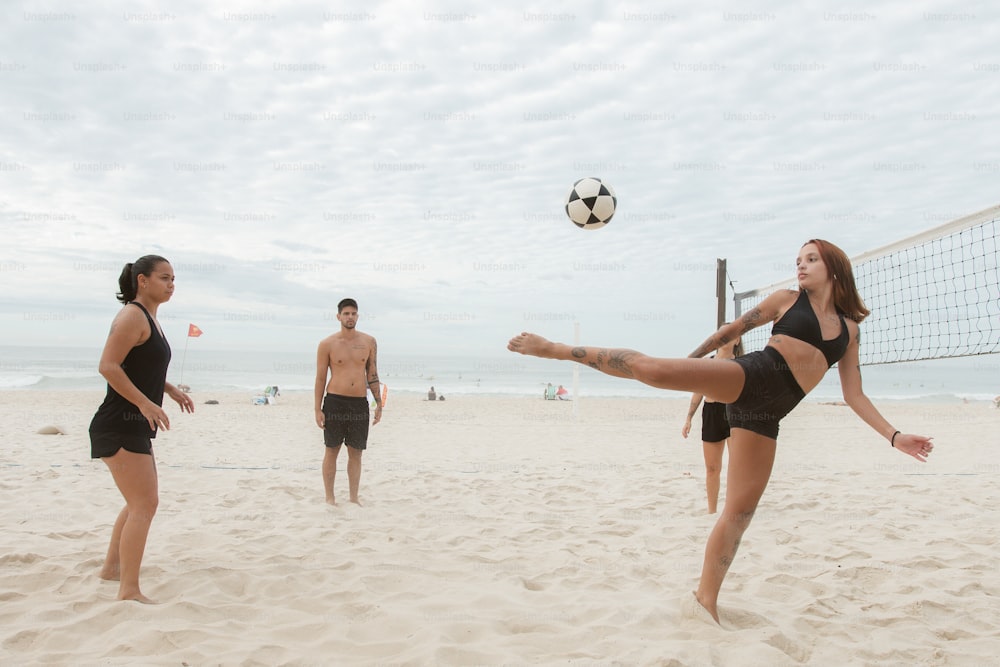 a woman kicking a volleyball ball across a beach