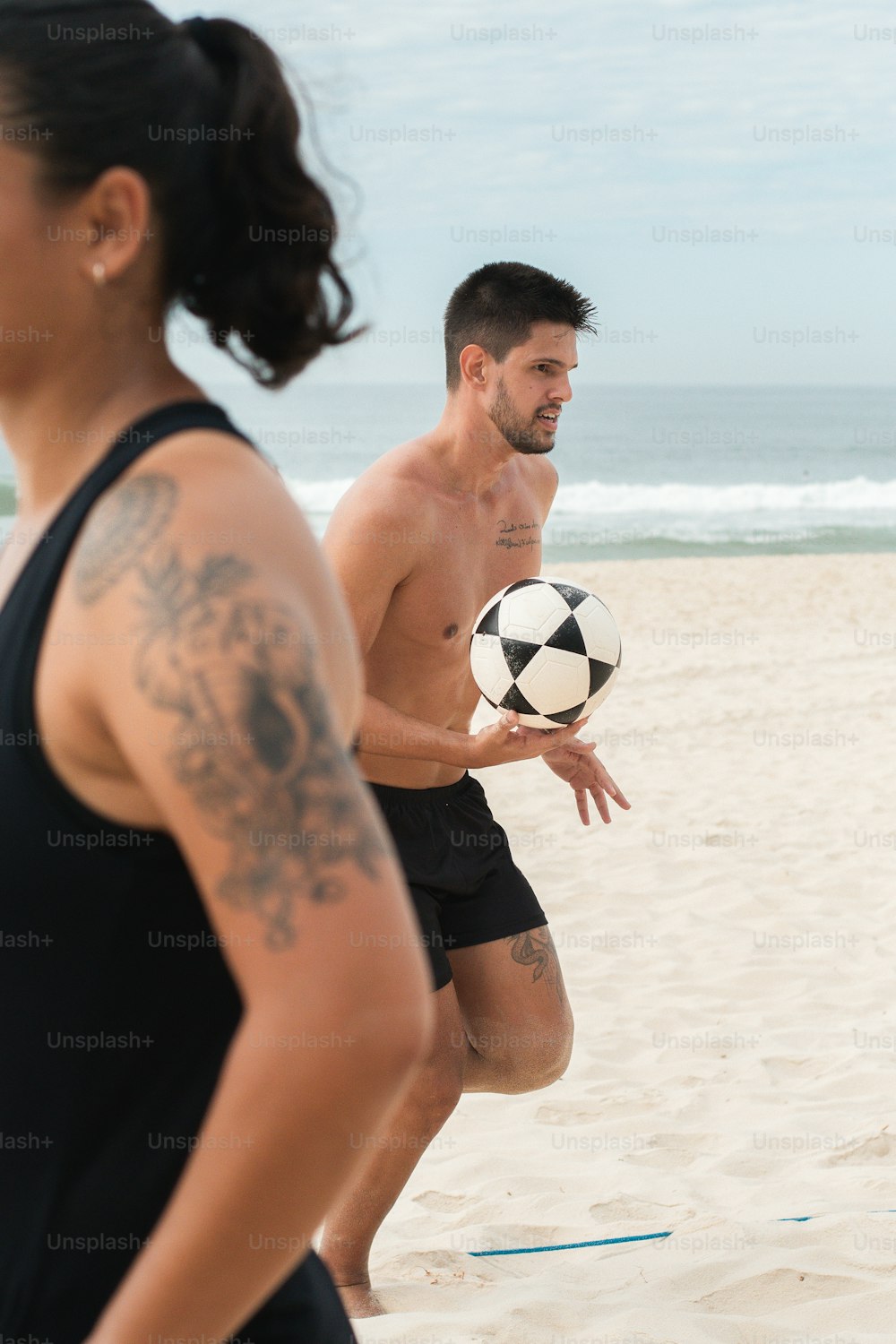 a man and a woman playing soccer on the beach