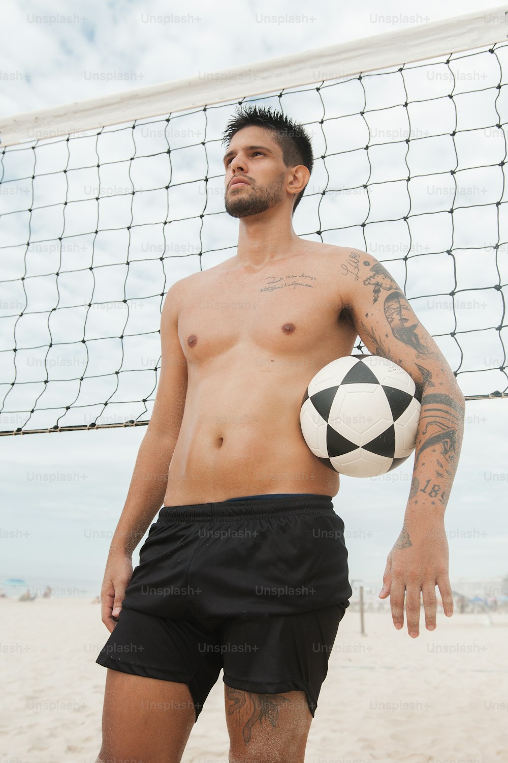 a shirtless man holding a soccer ball on a beach