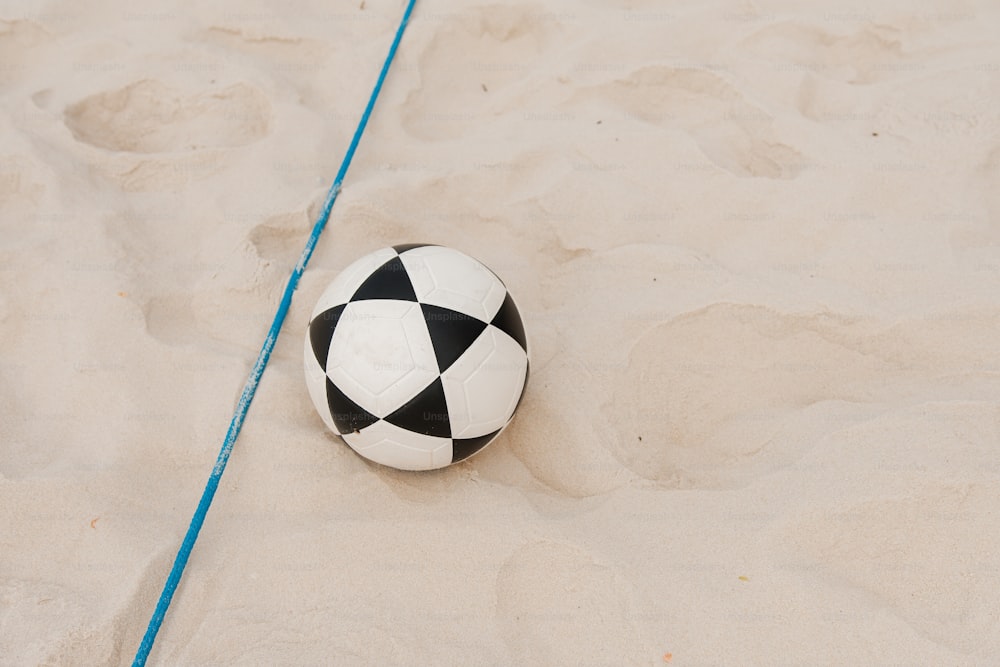 un ballon de football noir et blanc assis au sommet d’une plage de sable