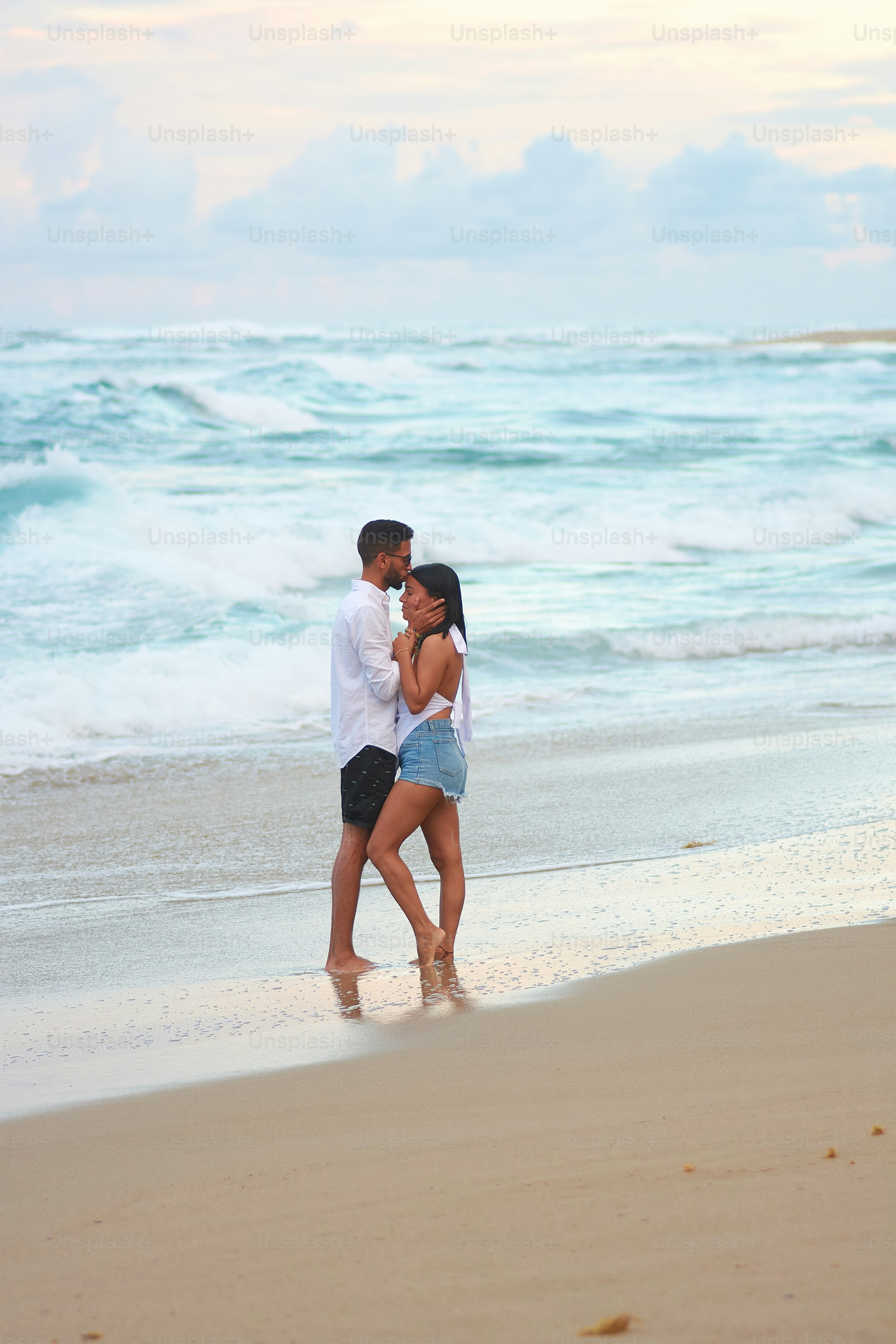 a man and a woman standing on a beach next to the ocean