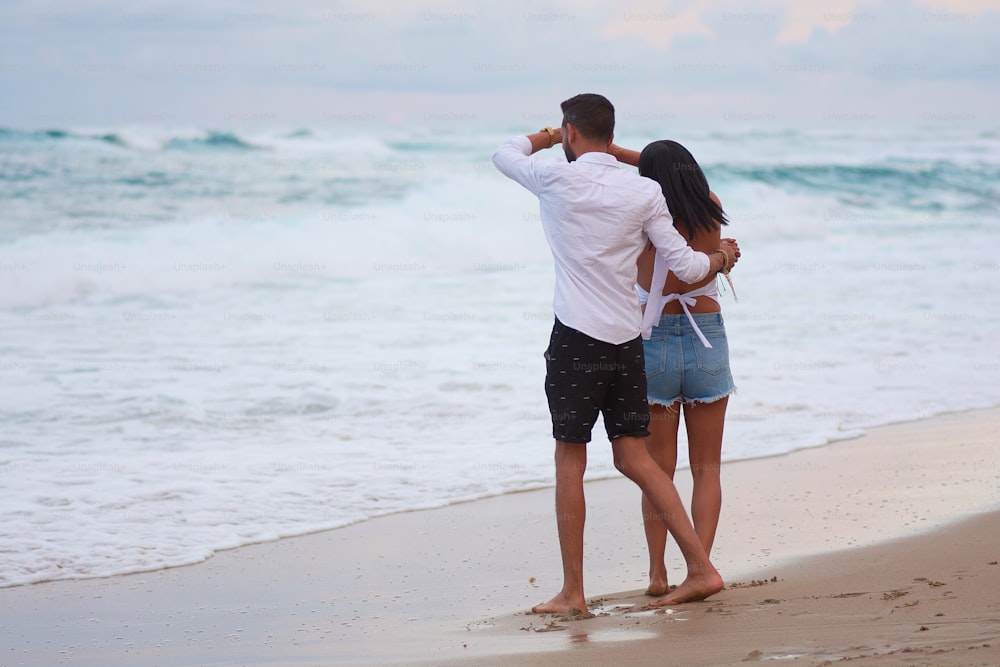 a man and woman standing on a beach next to the ocean