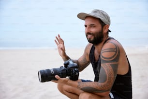 Un homme assis sur une plage tenant un appareil photo