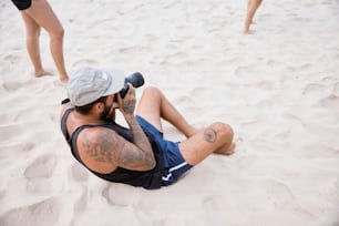 a man sitting in the sand talking on a cell phone