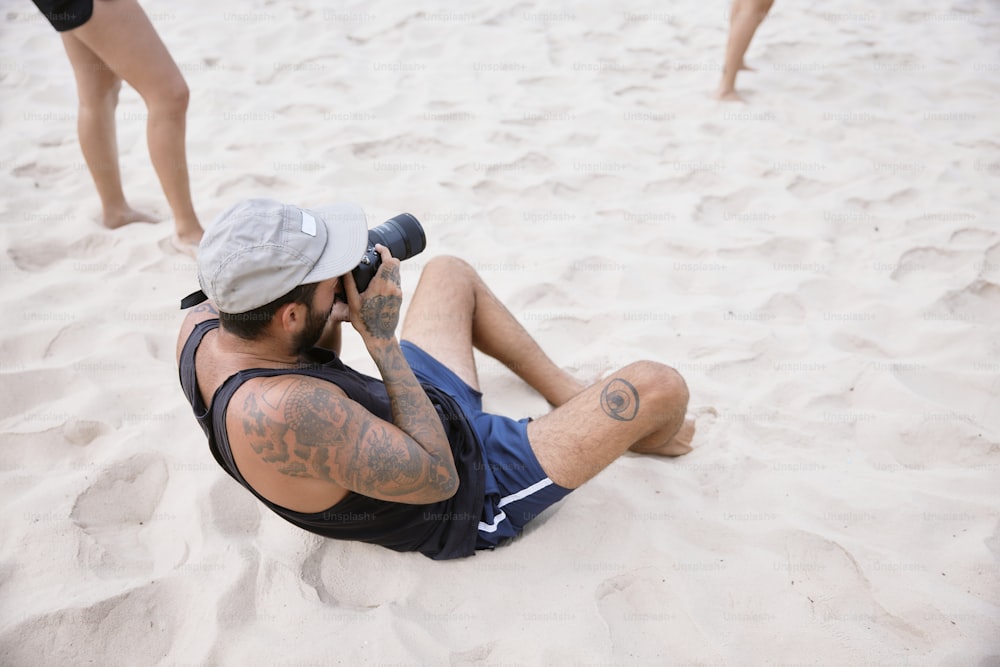 a man sitting in the sand talking on a cell phone