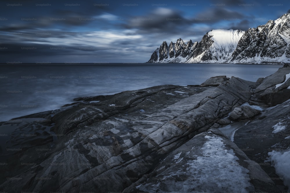 a rocky shore with snow covered mountains in the background