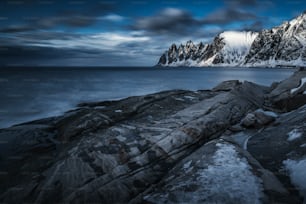 a rocky shore with snow covered mountains in the background