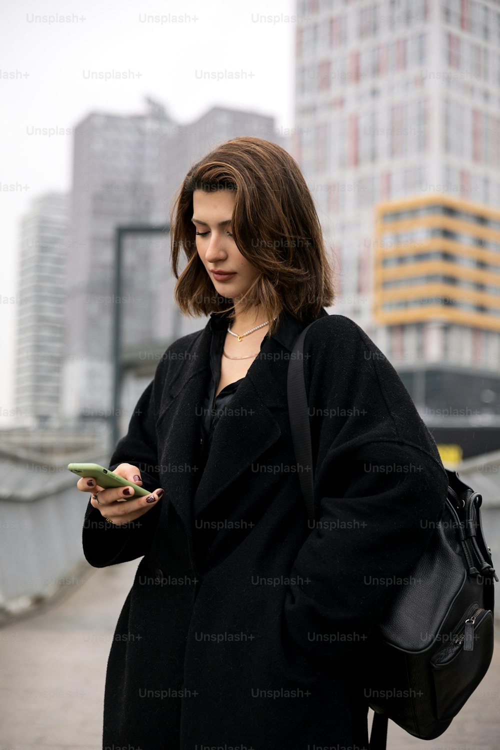 uma mulher em um casaco preto olhando para seu telefone celular