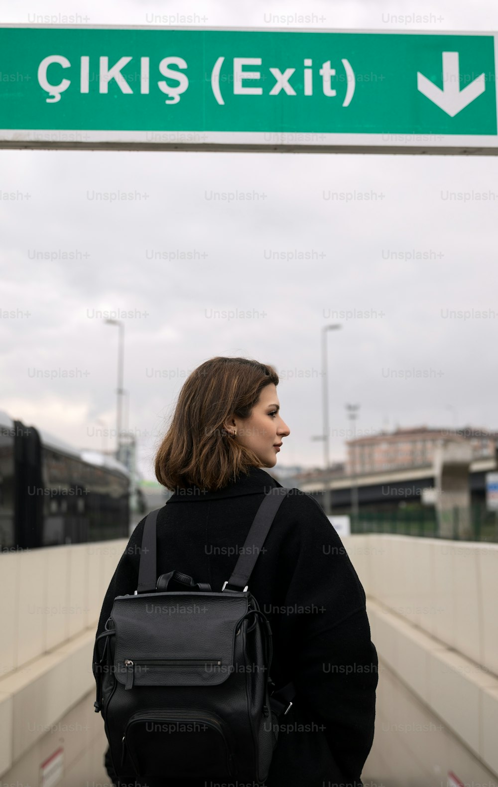 Eine Frau mit Rucksack steht unter einem Schild