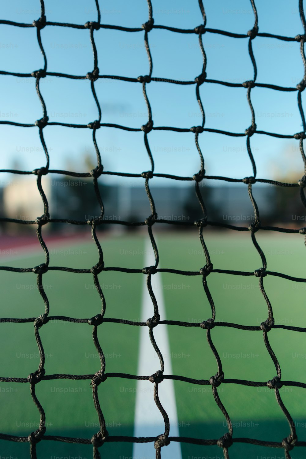 um close up de uma rede de tênis com uma quadra de tênis ao fundo