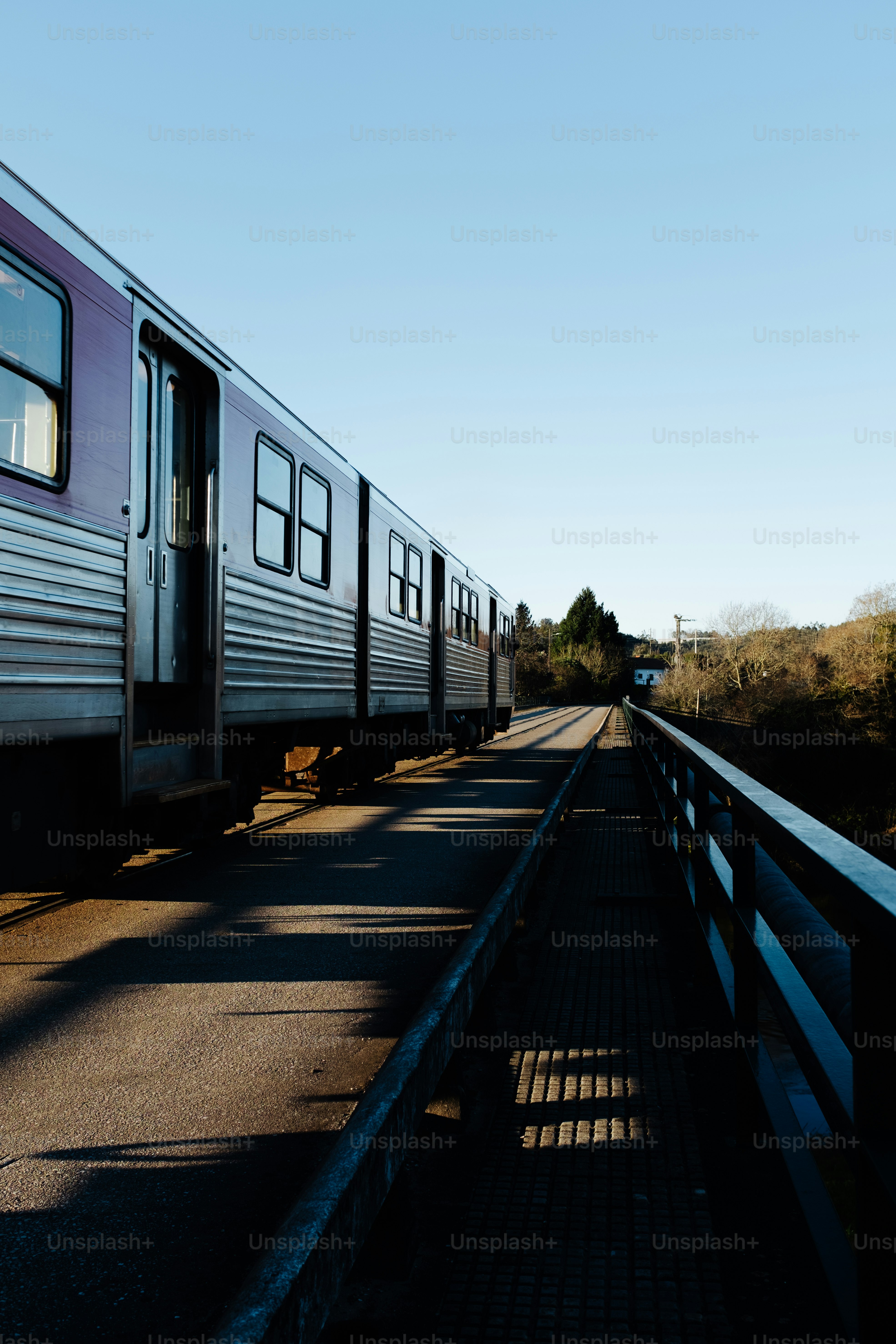 a silver train traveling down train tracks next to a forest