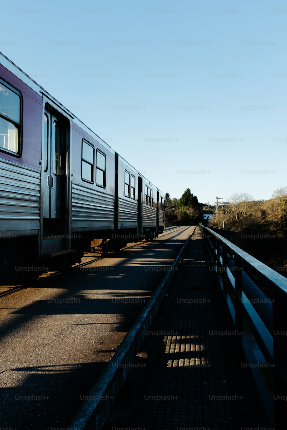 a silver train traveling down train tracks next to a forest