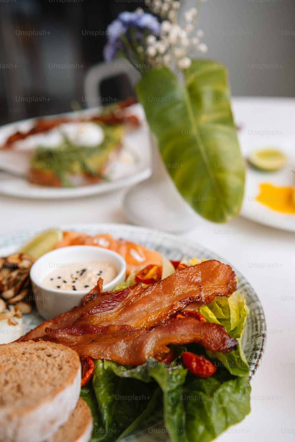 a plate with bacon, lettuce, toast, and other food items