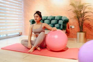 a woman sitting on a yoga mat with a pink ball