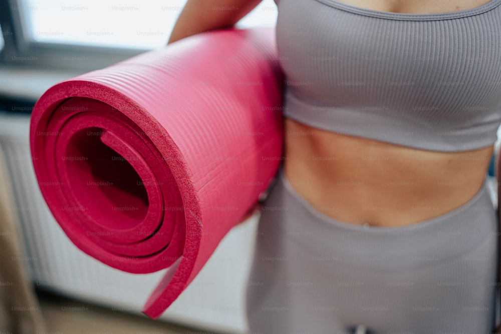 a woman holding a pink yoga mat in her right hand