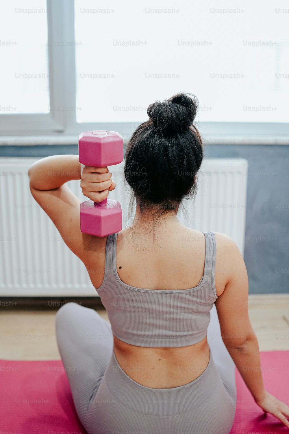 a woman sitting on a yoga mat holding a pink dumbbell