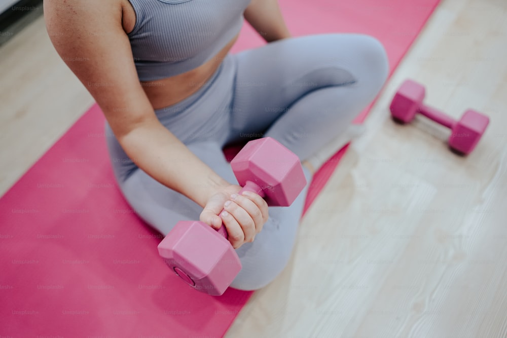 a woman sitting on the floor with a pink dumbbell