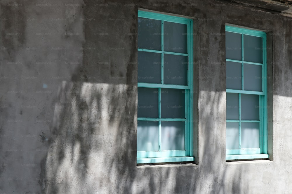two windows with green frames on a gray wall