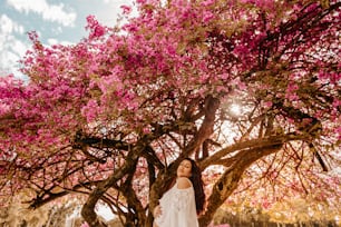 a woman standing under a tree with pink flowers