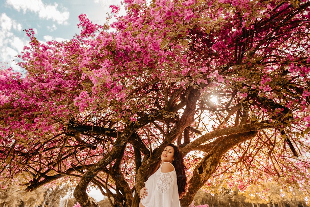 a woman standing under a tree with pink flowers