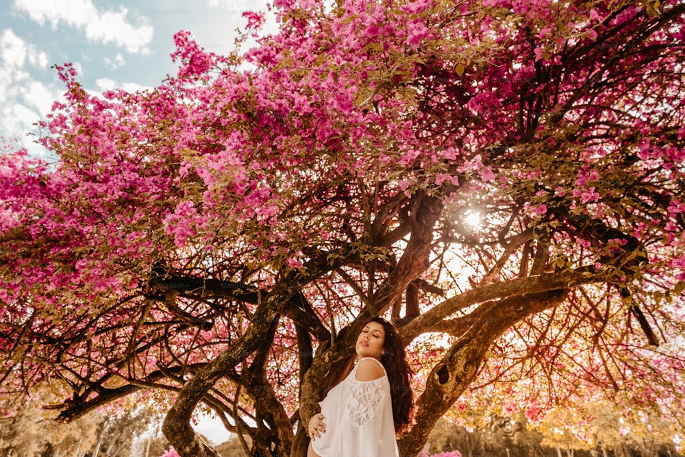 Una mujer parada debajo de un árbol con flores rosadas