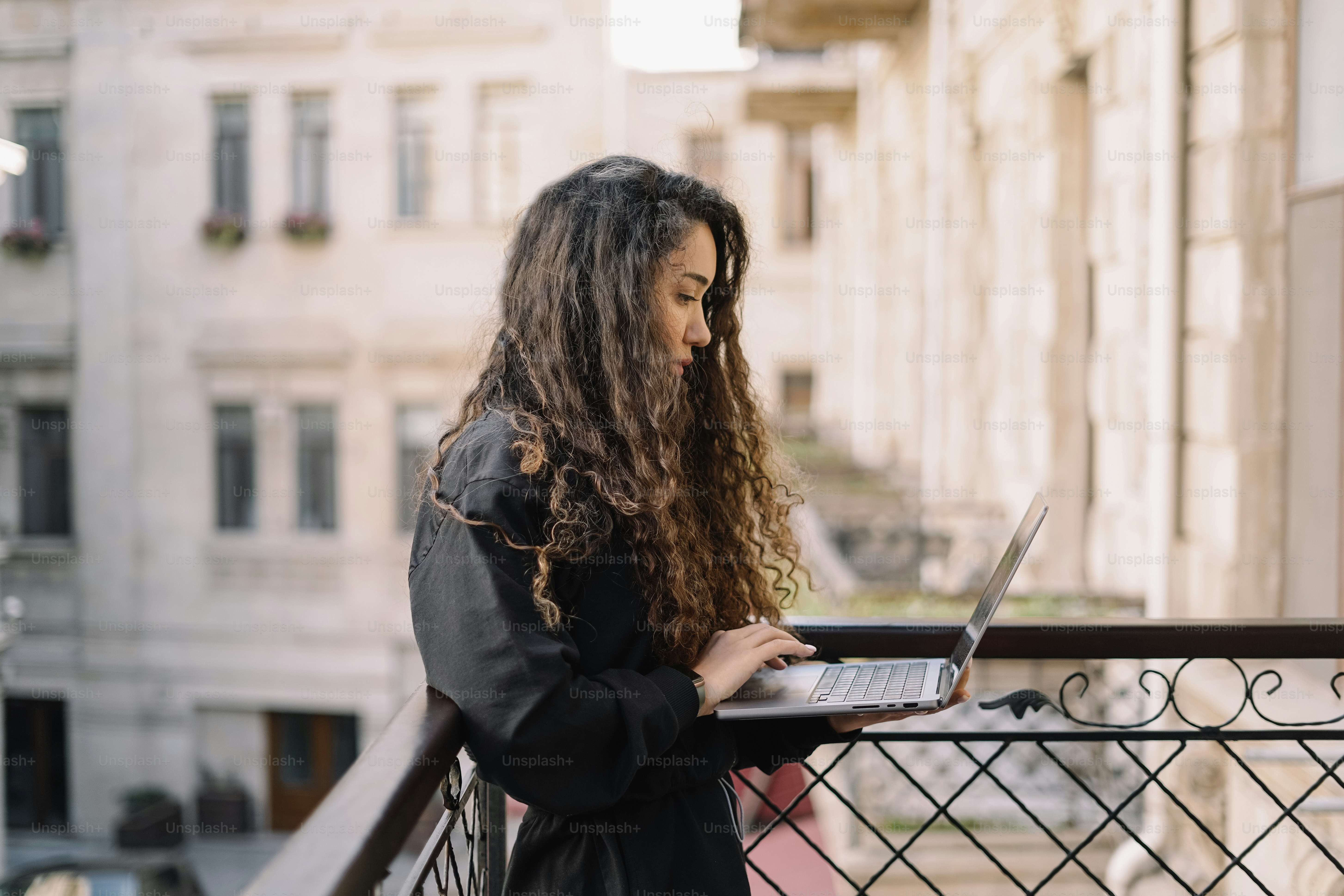 a woman standing on a balcony using a laptop computer